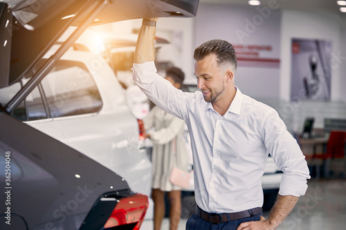 young caucasian customer man is opening car trunk in dealership  examine it before buying