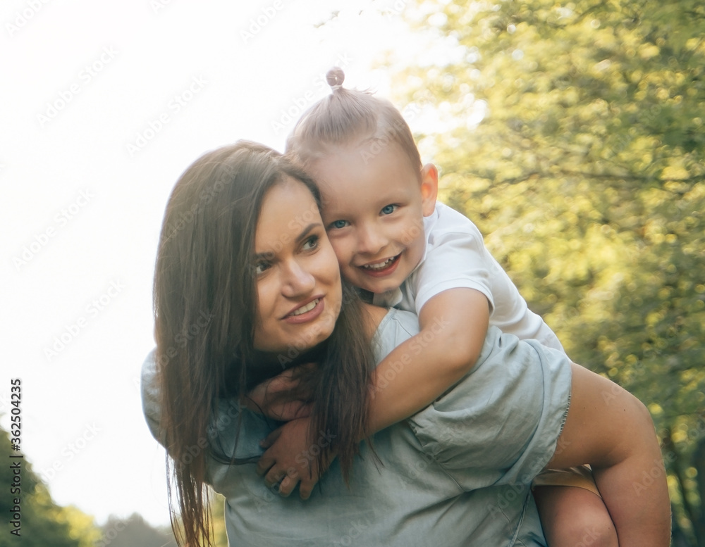 Portrait of a happy european mother and son. Caucasian woman and little toddler boy cuddling in a summer park on a sunny day on a green lawn. A happy family is playing. Close-up Portrait of a happy european mother and son. Caucasian woman and little toddler boy cuddling in a summer park on a sunny day on a green lawn. A happy family is playing. Close-up
