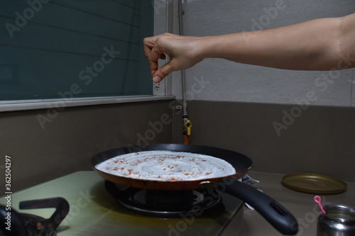sprinkling indian spices masala on hot dosa with hands on non stick pan