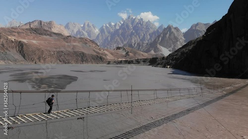 Aerial view of a man crossing the Hussaini suspension bridge over the Hunza river with the Passu Cones in the background, Gilgit Balistan region, Pakistan