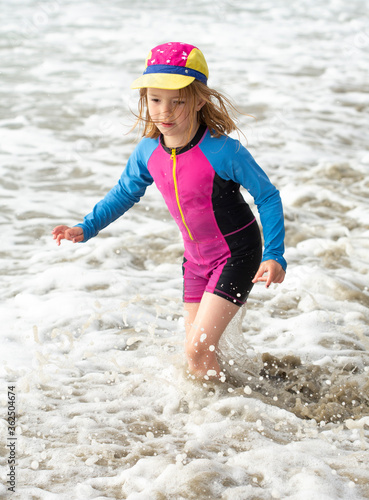 Fototapeta Naklejka Na Ścianę i Meble -  Young girl, 6 years old, in a brightly colored swimming suit, running and playing at the beach