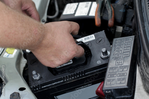 A man's hand takes the battery out of the car. Battery replacement.