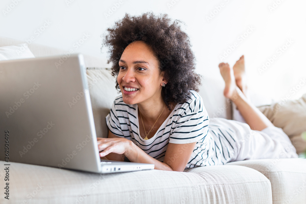 Young beautiful woman with curly hair working on laptop computer while sitting on the sofa at home, heck on oline shops for cyber monday sales. Technology woman concept alternative office freelance Young beautiful woman with curly hair working on laptop computer while sitting on the sofa at home, heck on oline shops for cyber monday sales. Technology woman concept alternative office freelance