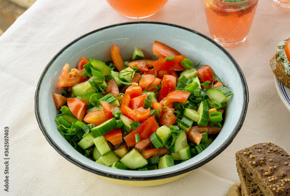 Summer vegetable salad with tomatoes, cucumbers and greens in iron bowl
