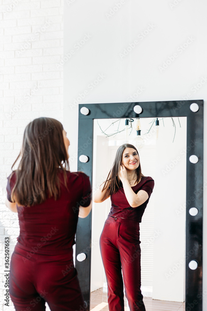 A girl in a red suit stands in front of a mirror, a large mirror, a reflection, trying on a suit, tailoring, outfit, going to a party or to a party A girl in a red suit stands in front of a mirror, a large mirror, a reflection, trying on a suit, tailoring, outfit, going to a party or to a party