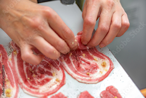 Woman hostess rolls thinly sliced bacon into roll for further cooking and frying in a pan. Cooking junk and fatty foods.