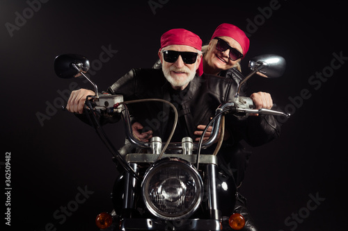 Photo of two cool old bikers grey hair man lady couple drive vintage chopper traveling together feel young wear rocker leather jacket outfit bandana isolated black color background