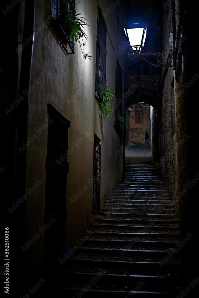 Alley with a staircase going up illuminated by a slight light from a lamppost