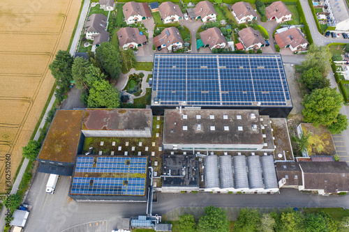 Aerial view of small factory with solar roofs surrounded by residential buildings