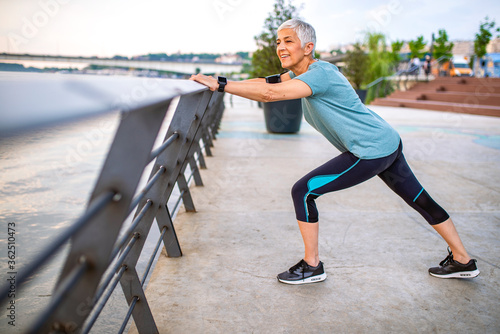 Senior woman exercising in park. Senior woman doing her stretches outdoor. Athletic mature woman stretching after a good workout session. Mature woman warming up before jogging