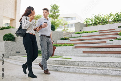 Emotional young businesswoman actively gesturing and talking to colleague when thay are walking in the street