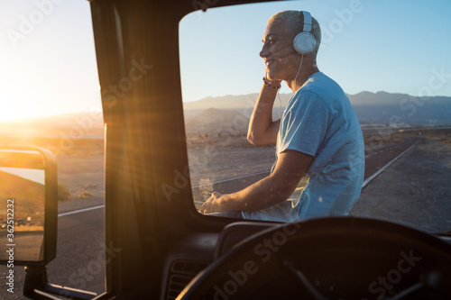 one man alone listening music with his headphones on his car looking at the beautiful landscape sunset - happy cheerful teenager travelling and using his phone on his holiday © Daniel