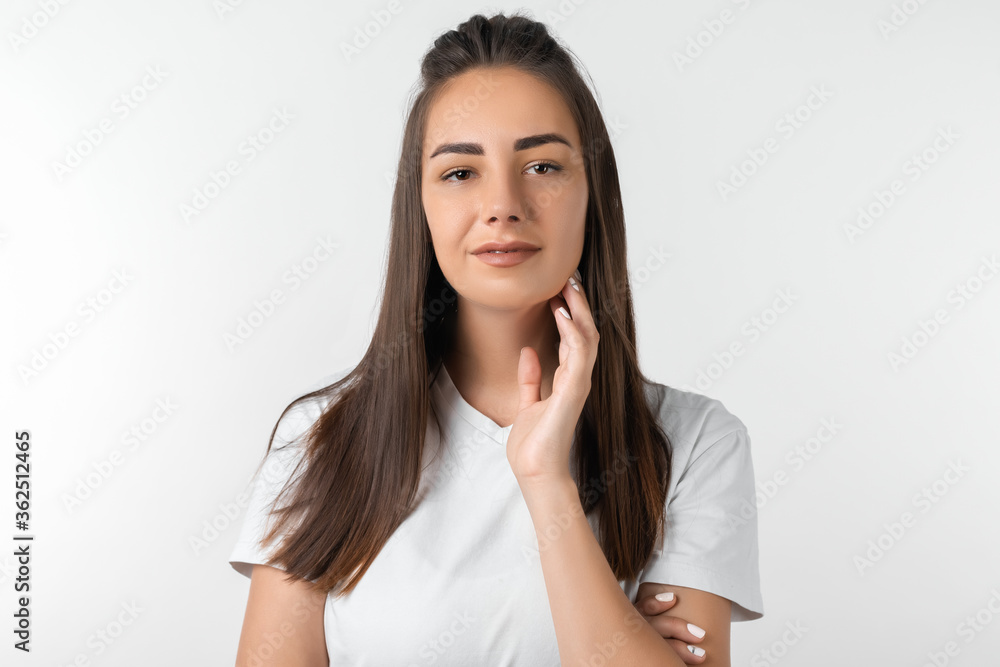 Picture of stylish Attractive European young woman with long chestnut hair keeps hand on neck. European young woman isolated over white background.