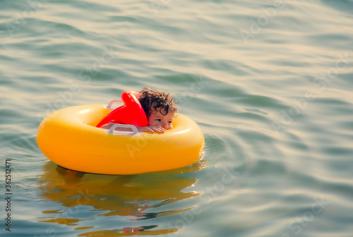 Happy little boy in a life jacket sitting in a big yellow swimming circle swims in the sea. Copy space