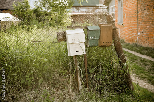 Vintage rustic mailboxes of different colors pinned on a fence.