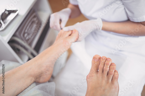 Pedicurist doing professional medical pedicure procedure in beauty salon with special eguipment. Foot treatment in SPA salon. Podiatry clinic. Beautician doctor hands in white gloves with female legs