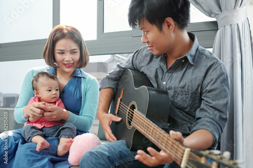 Vietnamese young man playing guitar and singing for his little daughter