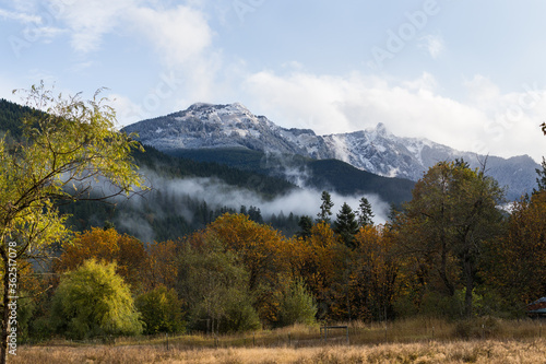 View on snowy mountains clouds and autumn colors forest. Changing season landscape