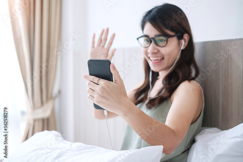 Happy casual woman making video calling by smartphone at home, young adult asian female using meeting online app on bed. social distancing, new normal, work from home, remotely and technology concept