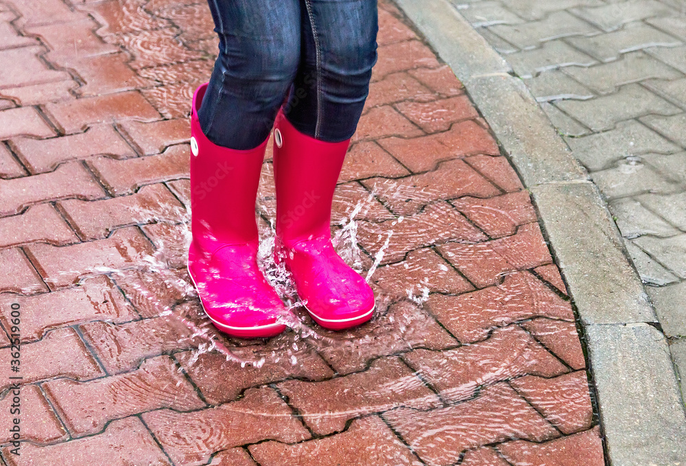 Autumn. Protection in the rain. Girl wearing pink rubber boots jumping into a puddle with splash. Autumn. Protection in the rain. Girl wearing pink rubber boots jumping into a puddle with splash.