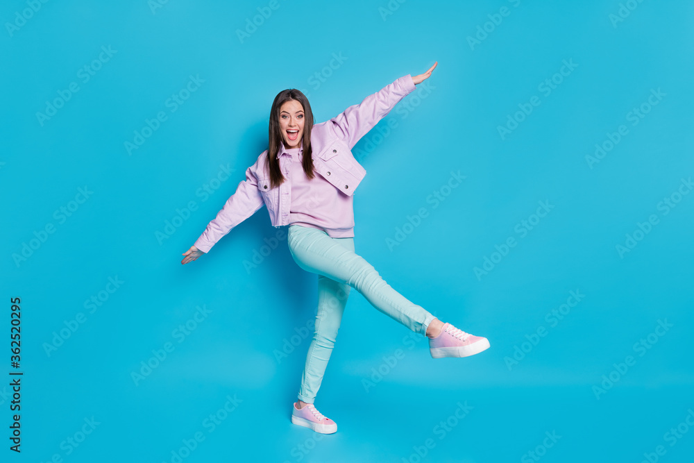 Full size photo of pretty lovely content girl raise hands legs enjoy spring holiday free time wear good look clothes gumshoes isolated over blue color background