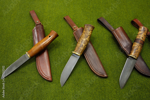 Close-up of handmade knives and leather sheathes placed on a tablecloth photo