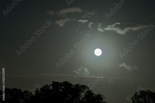 Scenic view of full moon with clouds. Planet Jupiter with moons is right above the large bright moon.