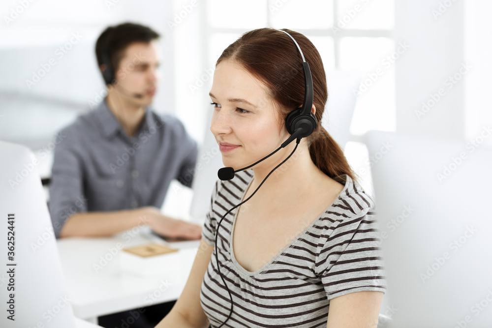 Casual dressed young woman using headset and computer while talking with customers online. Group of operators at work. Call center, business concept Casual dressed young woman using headset and computer while talking with customers online. Group of operators at work. Call center, business concept