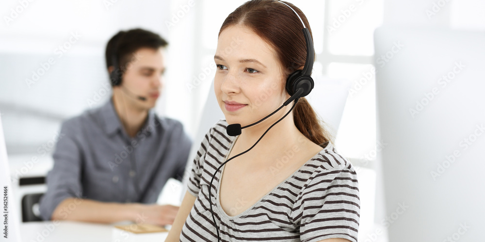 Casual dressed young woman using headset and computer while talking with customers online. Group of operators at work. Call center, business concept Casual dressed young woman using headset and computer while talking with customers online. Group of operators at work. Call center, business concept