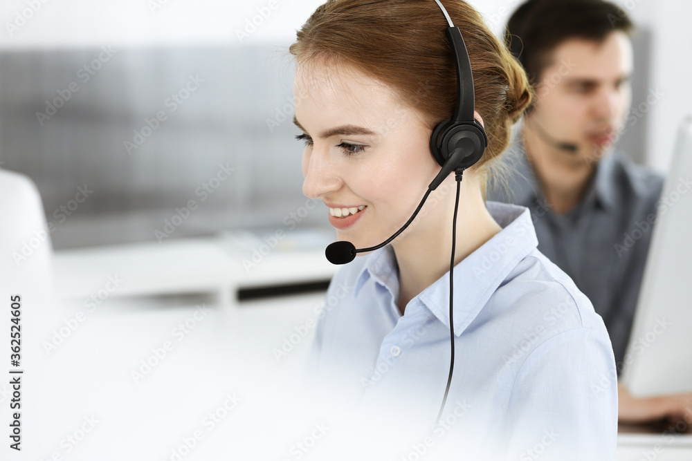 Young woman using headset and computer while talking with customers online. Group of Call center operators at work. Business concept Young woman using headset and computer while talking with customers online. Group of Call center operators at work. Business concept