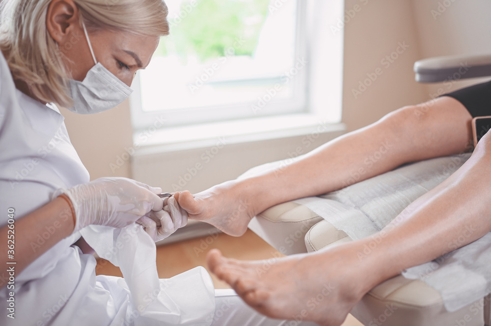Professional medical pedicure procedure using nail clippers instrument. Patient visiting chiropodist podiatrist. Foot treatment in SPA salon. Podiatry clinic. Pedicurist hands in white gloves.
