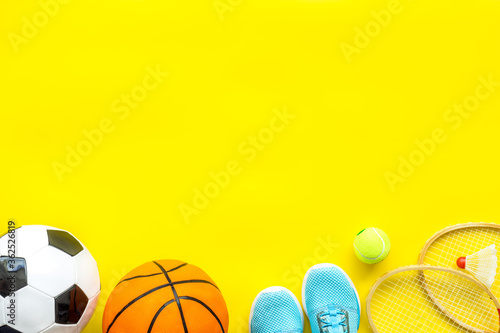 Sport games equipment - balls, sneakers, rockets - on yellow top view copy space