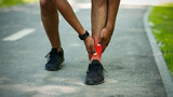 Unrecognizable young jogger feeling pain in his ankle during his morning run at park, close up