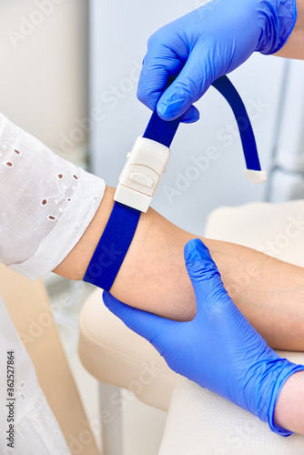 girl gives blood. doctor put a medical tourniquet on his arm