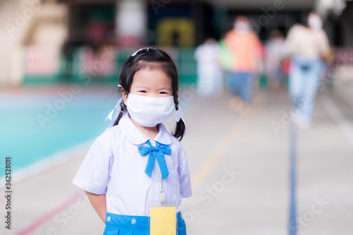 Asian girl wearing a white cloth mask to protect against the virus. She wore a school uniform, a blue skirt standing on a cement field. Concept: Children back to school in corona virus outbreak.