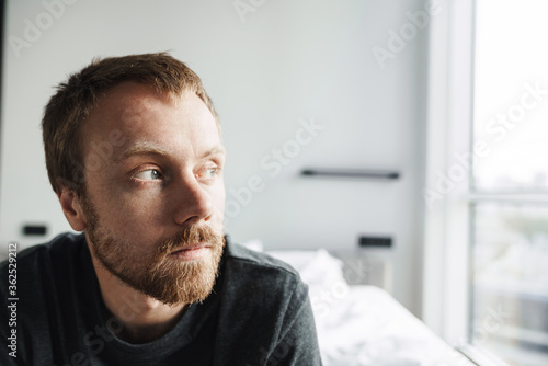 Photo closeup of redhead man looking aside while sitting on bed