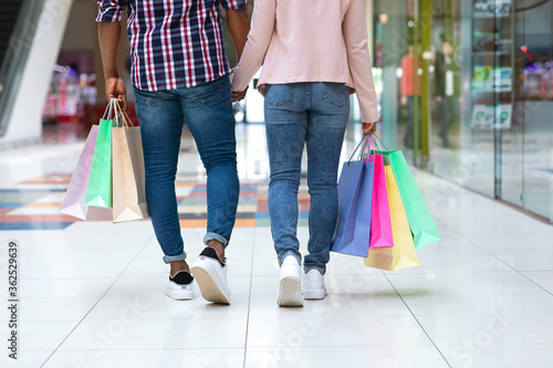 Young african american couple with shopping bags walking by mall center holding hands, panorama, back view, copy space