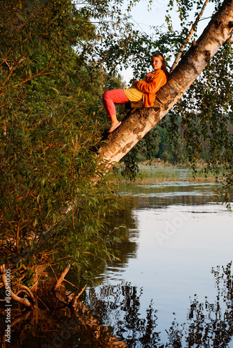 beautiful girl on a tree over water at sunset