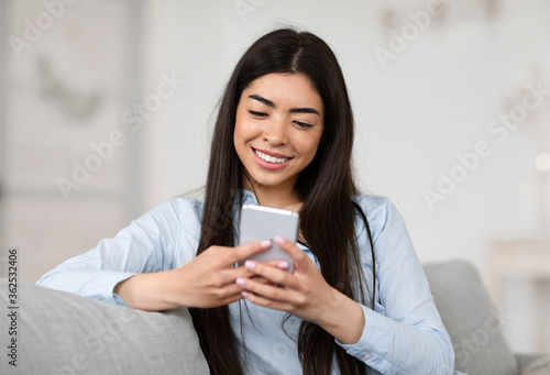 Smiling Asian Girl Browsing Social Networks On Smartphone At Home, Enjoying Weekend