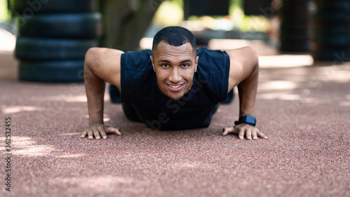 Black millennial sportsman doing push ups on jogging track at park