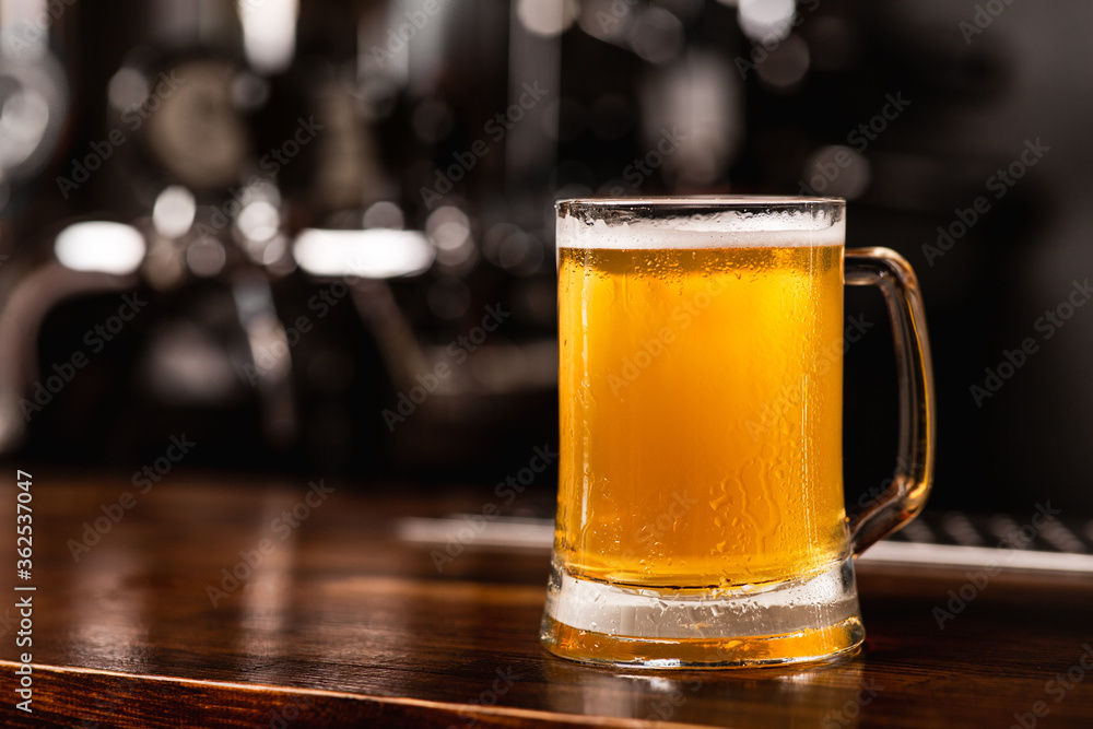 Favorite fresh beer from keg. Mug of light ale on wooden bar counter on blurred background