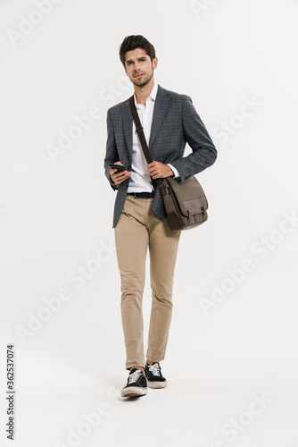 Photo of young businessman using cellphone while walking with bag