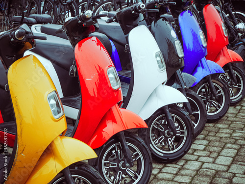 Multicolored electric mopeds stand in a row on paving stones photo