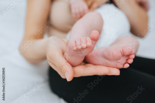 A loving, caring mother holds in her palm the legs of a small sleeping baby close-up. Woman's happiness. Photography, concept.