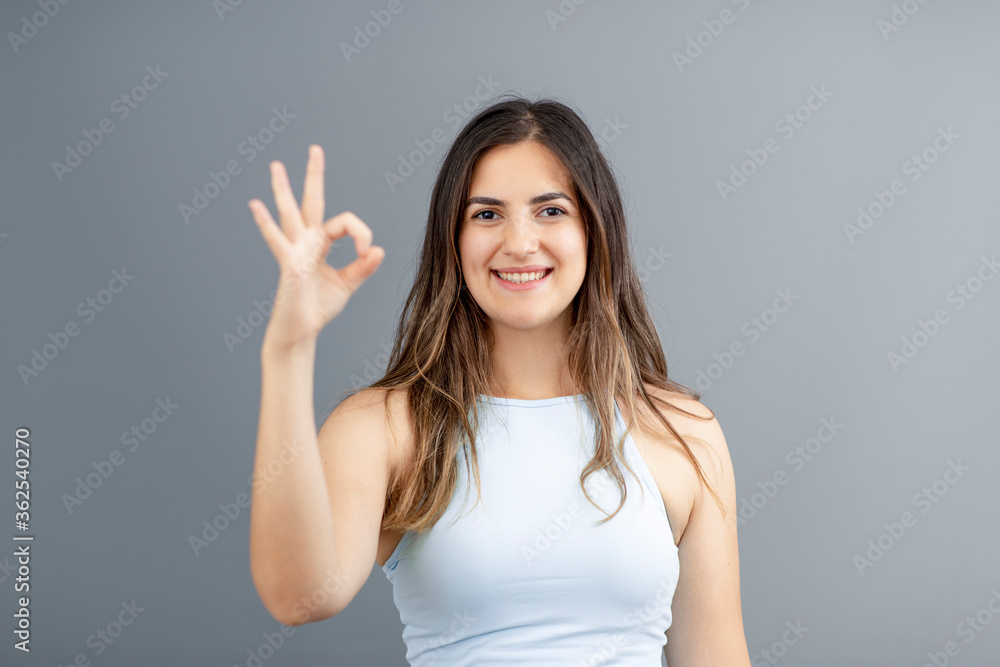 Beautiful brunette Turkish woman making an okay gesture with her hand, grey background studio shot with copy space Beautiful brunette Turkish woman making an okay gesture with her hand, grey background studio shot with copy space