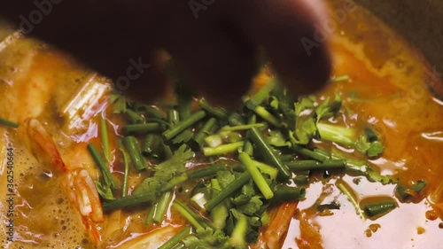 Someone put a coriander and spring onion on a pot of River prawn spicy soup. Tom Yam Goong. Traditional Thai food. Close up. Slow motion. Hot Soup and seafood menu. 