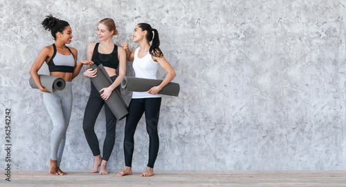 Pilates Class. Sporty Young Girls Standing With Yoga Mats Near Gray Wall