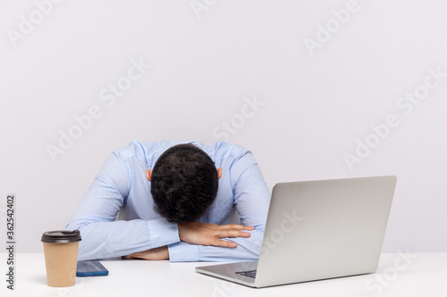 Upset tired man, office employee lying on table, sleeping at workplace, dozing off exhausted bored, decided to take nap during overtime night shift. indoor studio shot isolated on white background