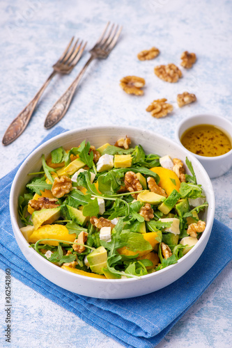 Arugula salad with peaches, avocado, camembert and walnuts, on light backgound.