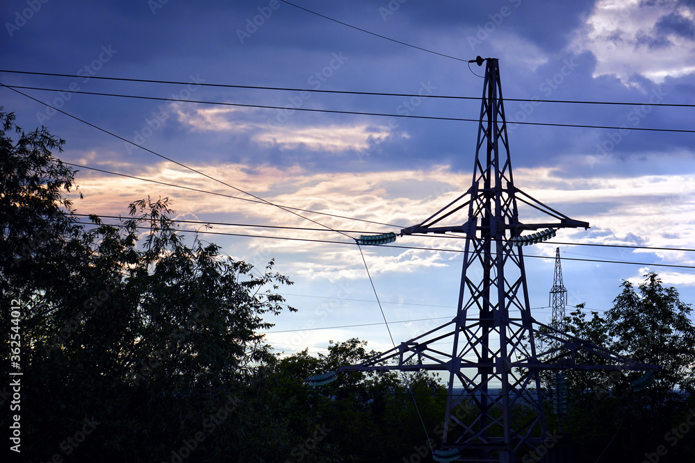Silhouette of a high-voltage power line tower against a cloudy sky in the evening